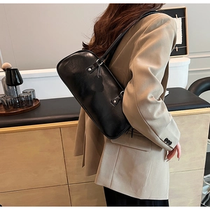 Glossy black underarm bag worn with beige blazer, showing minimalist commuting style