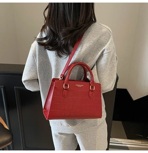 Detail view of red crocodile-patterned handbag with golden hardware and fashion lettering