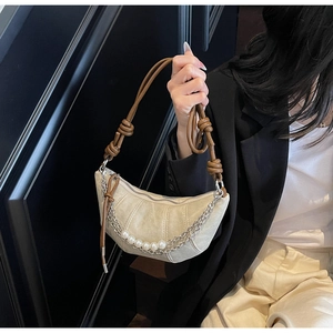 Detail of beige crescent bag featuring pleated leather texture and a knotted brown strap