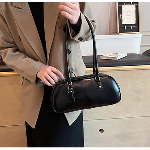 Minimalist black oval underarm bag with a cute cat charm shown on model in a cozy room