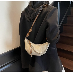Close-up of beige crescent bag with decorative metal chain and pearl strand detail
