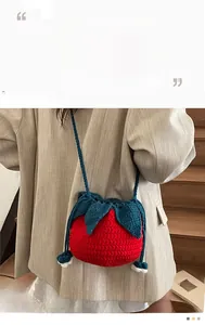 Detail of a handmade red strawberry-shaped knit crossbody bag with leaf lid and blue strap