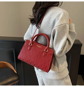 Detail of red quilted tote bag with gold lettering shown on a crossbody shoulder strap