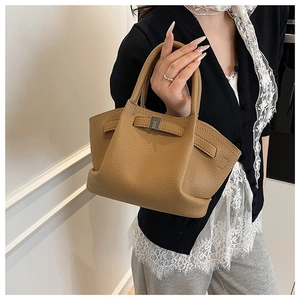 Close-up of brown litchi grain leather handbag with decorative strap and top handles