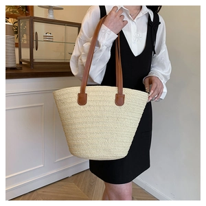 Woven straw tote bag detail showing beige texture and brown leather straps in use