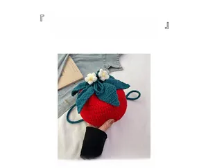 Detailed view of red knitted tomato shoulder bag with green leaves and white flowers