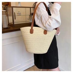 Close-up of woven straw tote bag with brown leather straps and detailed stitching