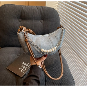 Close-up of denim crescent bag featuring contrast stitching and pearl chain strap detail