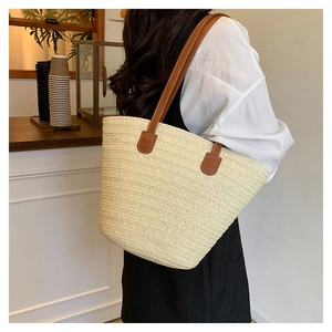 Large beige straw tote bag with brown leather straps shown on shoulder in a cafe
