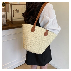 Detail of hand-woven straw tote bag featuring premium brown leather shoulder straps