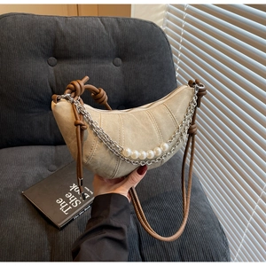 Detail of beige crossbody croissant bag with woven shoulder strap and silver chain decor