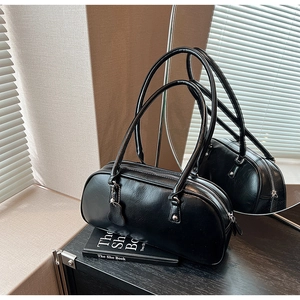 Close-up of glossy black leather cylinder bag with silver zipper and long shoulder straps