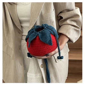 Detail of a handmade red strawberry crochet bag with drawstring closure and green leaf detail