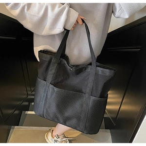 Detalle del bolso tote de lona negra de gran capacidad con bolsillos frontales de malla