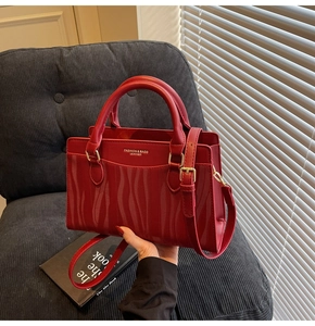 Detail of red bridal tote bag with wave texture and golden logo on a velvet chair