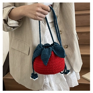 Detail showing red strawberry knitted bag with drawstring closure and leaf accents