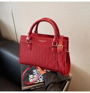 Detail of red quilted tote bag with gold buckle strap on fashion books in studio