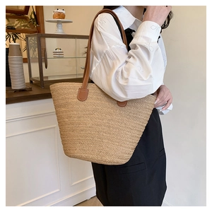 Detail of straw woven tote bag with leather straps on model shoulder in a cafe