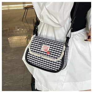 Detail of checkered canvas bag with lace trim, ribbon bow, and strawberry charm accessory