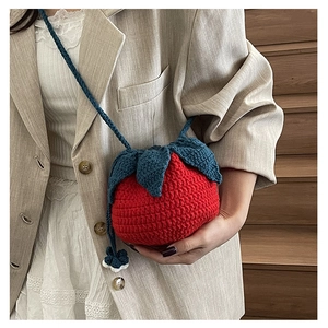 Close-up of handmade red strawberry knit shoulder bag with green leaf top detail