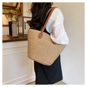 Detail of woven straw tote bag with brown leather handles and reinforced stitching for travel