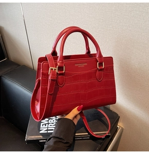 Detail of dark red crocodile pattern leather handbag with gold metal buckles and handles