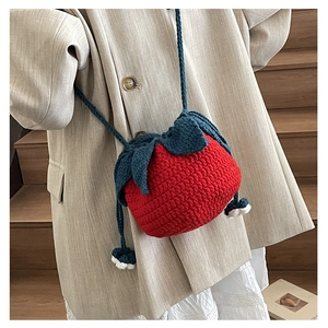 Detailed close-up of a red strawberry-shaped knitted shoulder bag with leaf drawstring