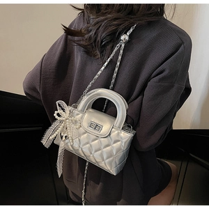 Detail of silver quilted mini bag with elegant pearl and lace bow charm accessories