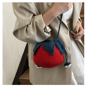 Close-up of handmade strawberry-shaped knitted shoulder bag worn with a beige suit