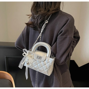 Detail of silver quilted handbag with metal handle, lace bow and pearl bead charms
