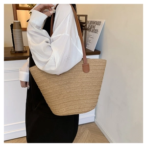 Detail of a woven straw tote bag with brown leather straps shown in a warm cafe setting