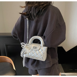 Detailed view of quilted silver chain bag with a lace bow and pearl charm on a model