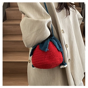 Close-up of handmade red strawberry knit shoulder bag with blue crochet leaf detail