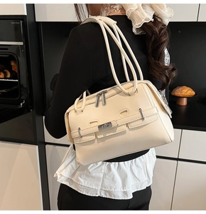 Model wearing a minimalist cream shoulder bag with silver hardware in a kitchen setting