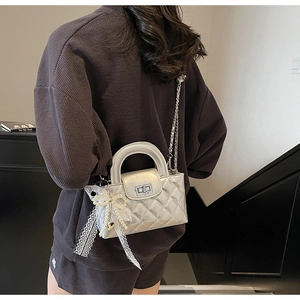 Close-up of silver quilted crossbody bag with white lace bow and pearl charm detail