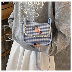 Detail of blue gingham crossbody bag featuring white lace trim and strawberry charm decoration