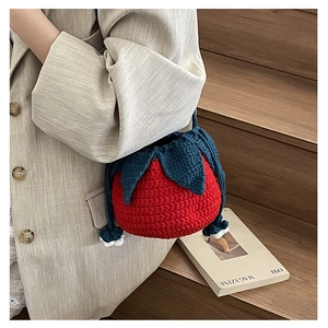 Close-up of handmade red crochet strawberry bag with blue leaf detail and knit texture
