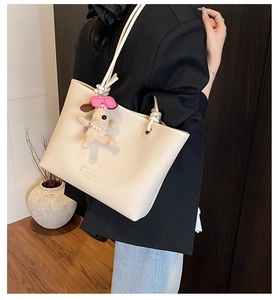 Detail of off-white lychee texture tote bag with plush puppy charm and embossed text