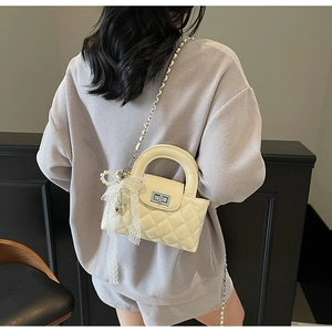 Detail of cream quilted crossbody bag with lace bow and pearl pendant on model