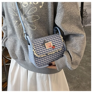 Detail of blue plaid canvas crossbody bag with white lace trim and strawberry patch
