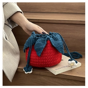 Macro view of handmade knitted strawberry bucket bag with drawstring and floral charm