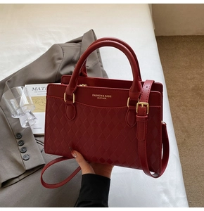 Detail of red leather tote bag with quilted pattern, gold hardware, and top handles