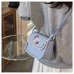 Detail of blue plaid canvas mini bag featuring lace trim and strawberry pendant on a model