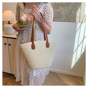 Detail of hand-woven beige straw tote bag with brown leather handle and stitching