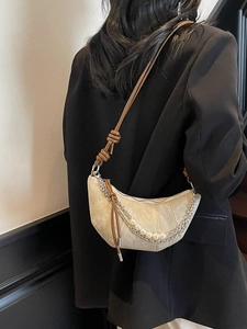Minimalist beige crescent bag with decorative pearl and metal chain straps on black blazer