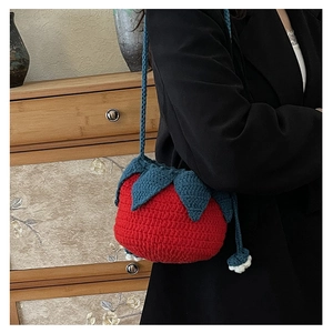 Detail of a handmade red knitted tomato-shaped shoulder bag with green leaf top cover