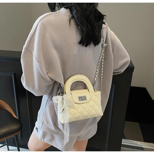 Macro detail of quilted crossbody bag with silver clasp and lace bow pendant accessory
