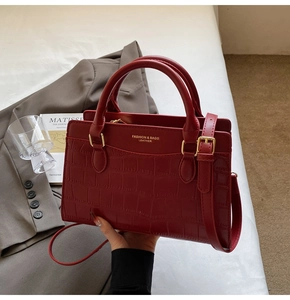 Detail of red croc-embossed handbag featuring gold logo and adjustable shoulder strap