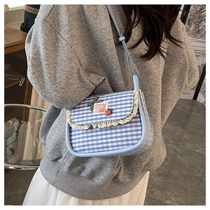 Detail of blue gingham crossbody bag with lace trim, bow, and strawberry charm