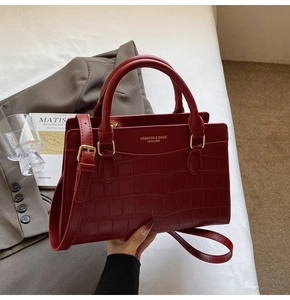 Detail of dark red crocodile embossed tote with golden logo and dual top handles